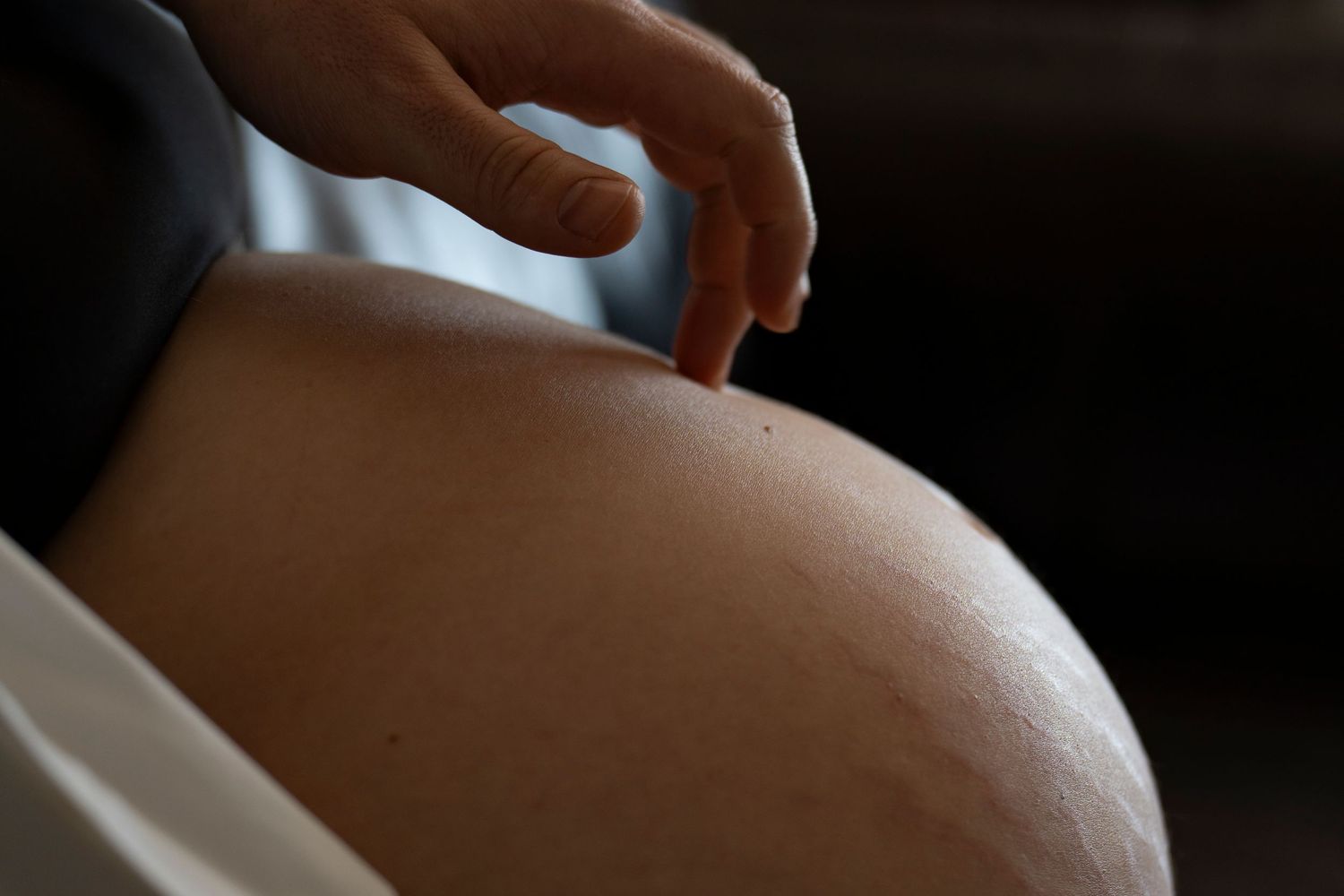 Close-up of a pregnant woman's bare baby bump with a hand gently touching the belly.
