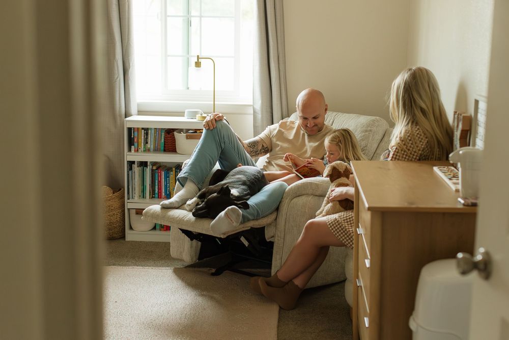 dad reading book with toddler in nursery chair with dog