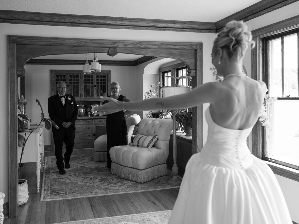 Black and white photo of a bride in a white gown surprising her parents during an emotional first look moment.