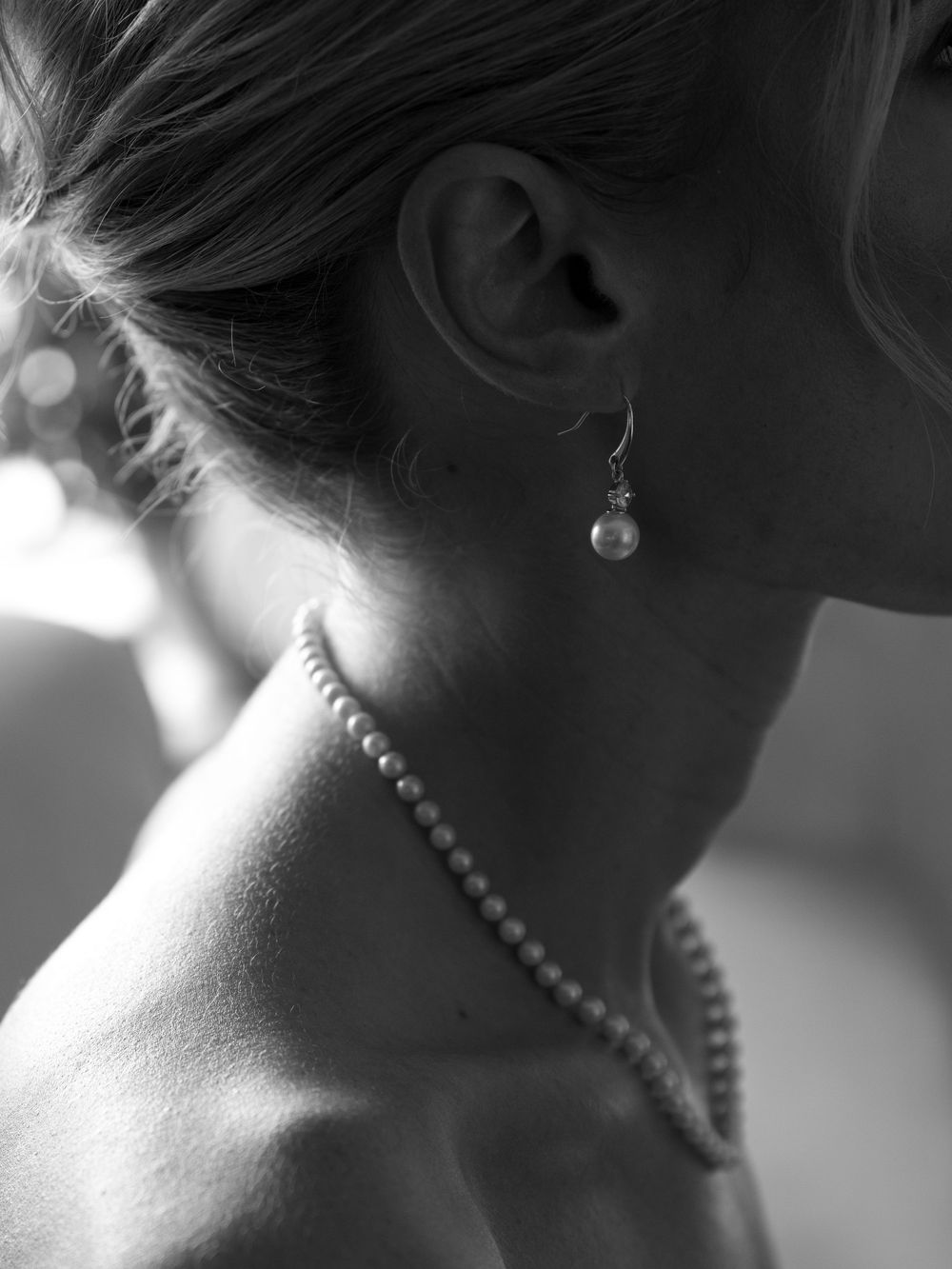 Close-up black and white photo of a bride wearing pearl earrings and a pearl necklace on her wedding day.