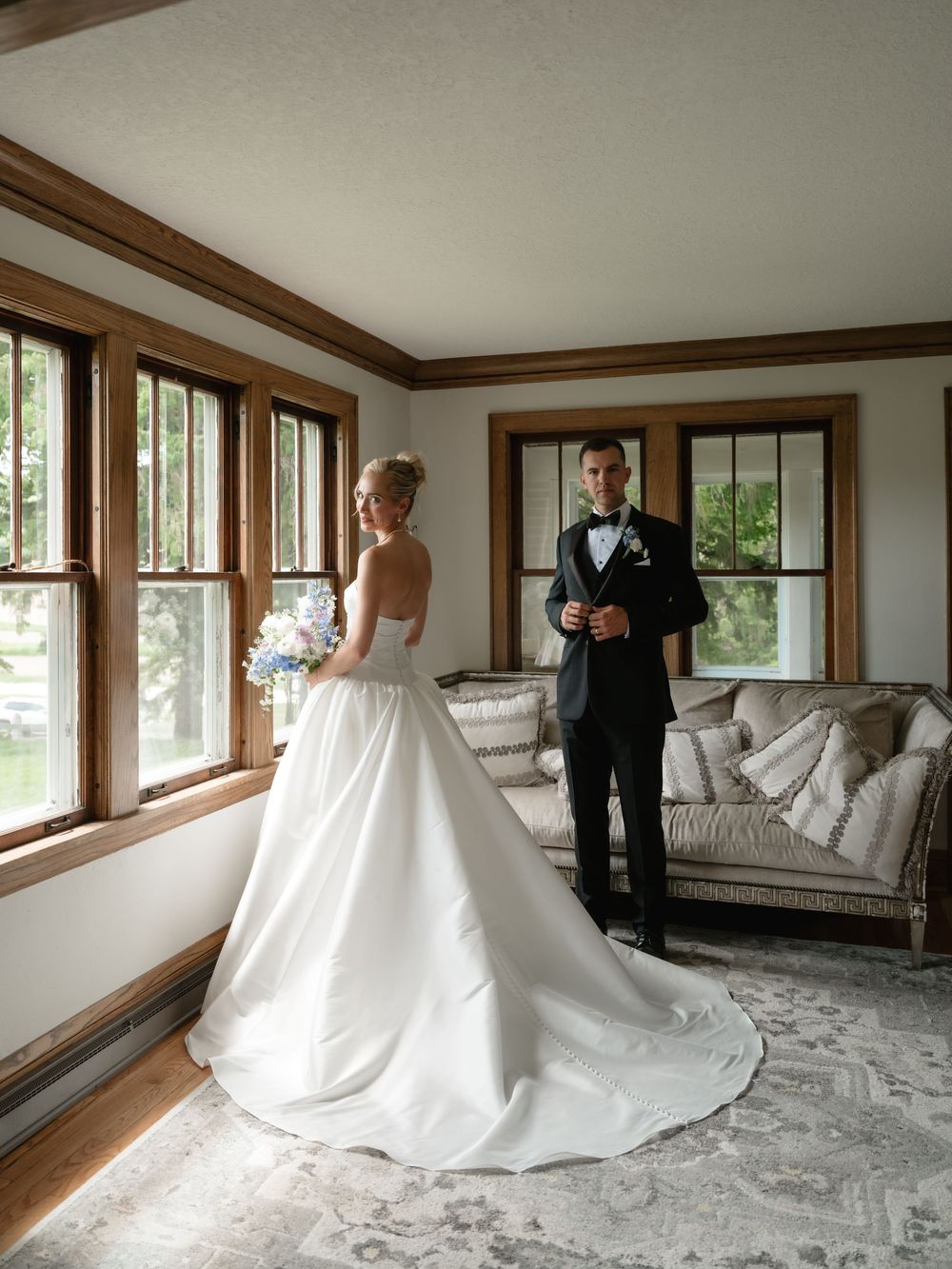 Bride in white ballgown and groom in black tuxedo share a first look moment in an elegant sunlit room.