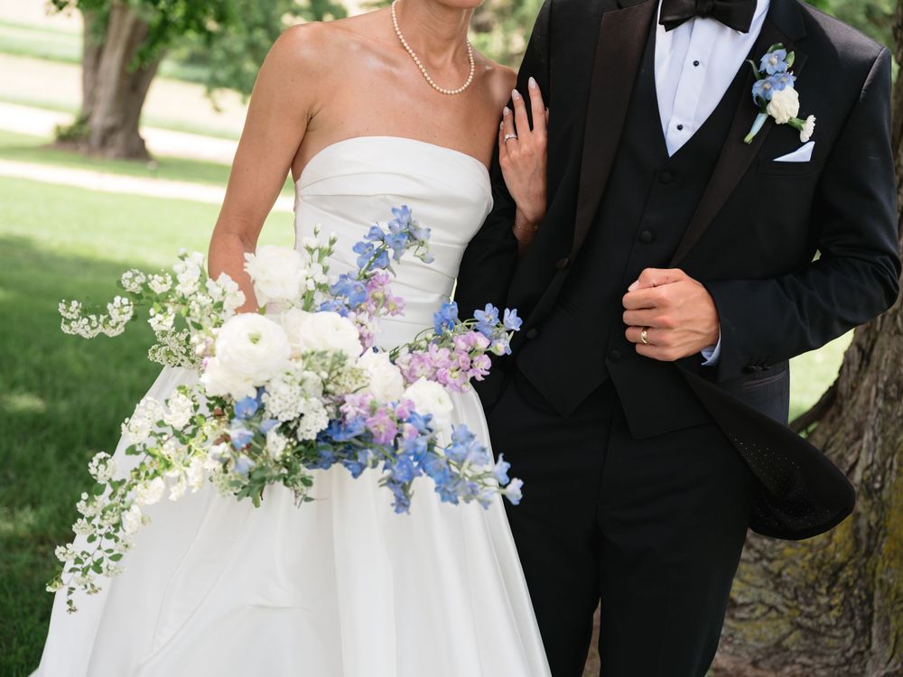 Bride and groom posing outdoors, bride holding a cascading bouquet of blue, white, and pink flowers.