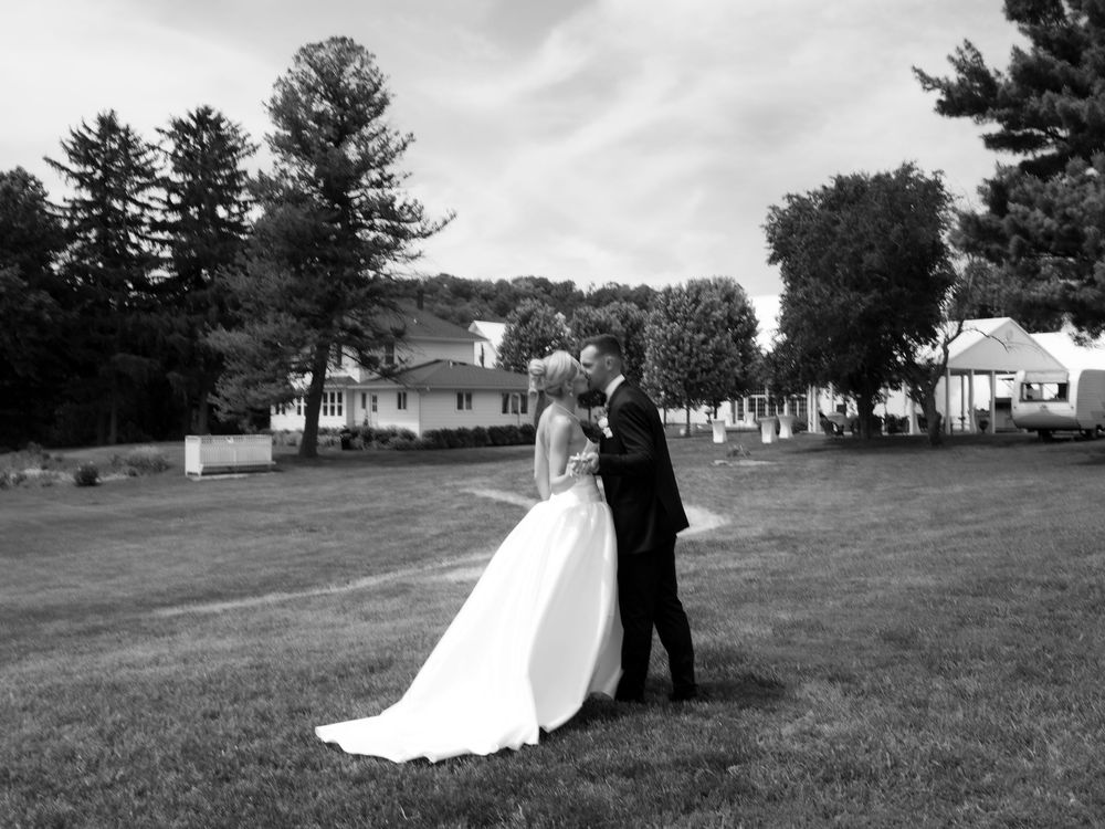 Black and white photo of a bride and groom sharing a kiss on a green lawn on their wedding day.