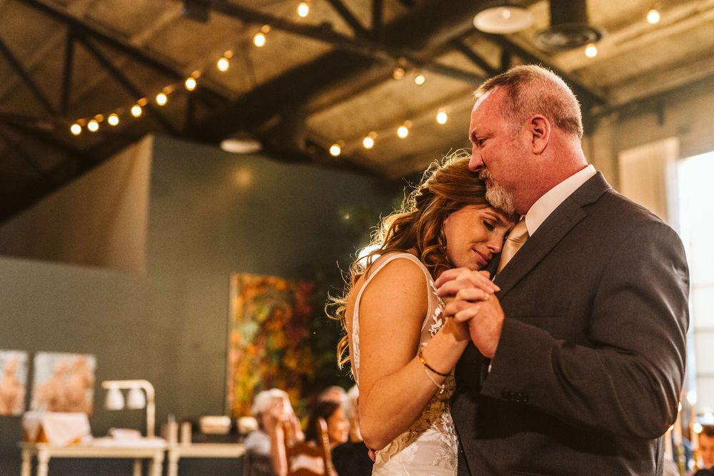 Bride and groom share an emotional first dance at a warmly lit wedding reception venue.