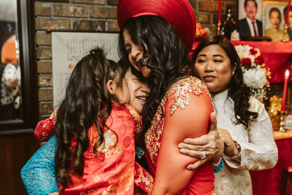 Women in traditional Vietnamese ao dai attire share a warm embrace during a festive wedding ceremony celebration.