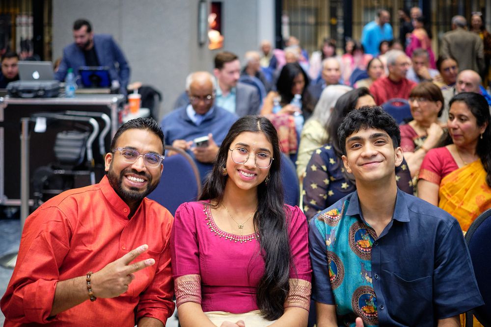 Three smiling friends in colorful traditional Indian attire pose together at a festive cultural celebration event.