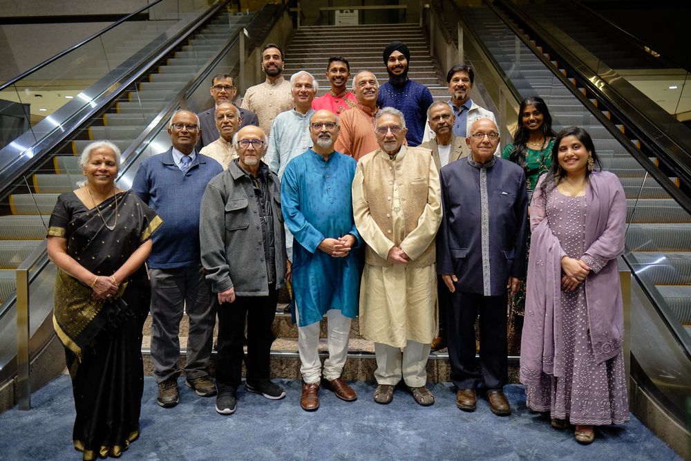 Group of people in formal and traditional Indian attire posing together on escalator steps indoors.
