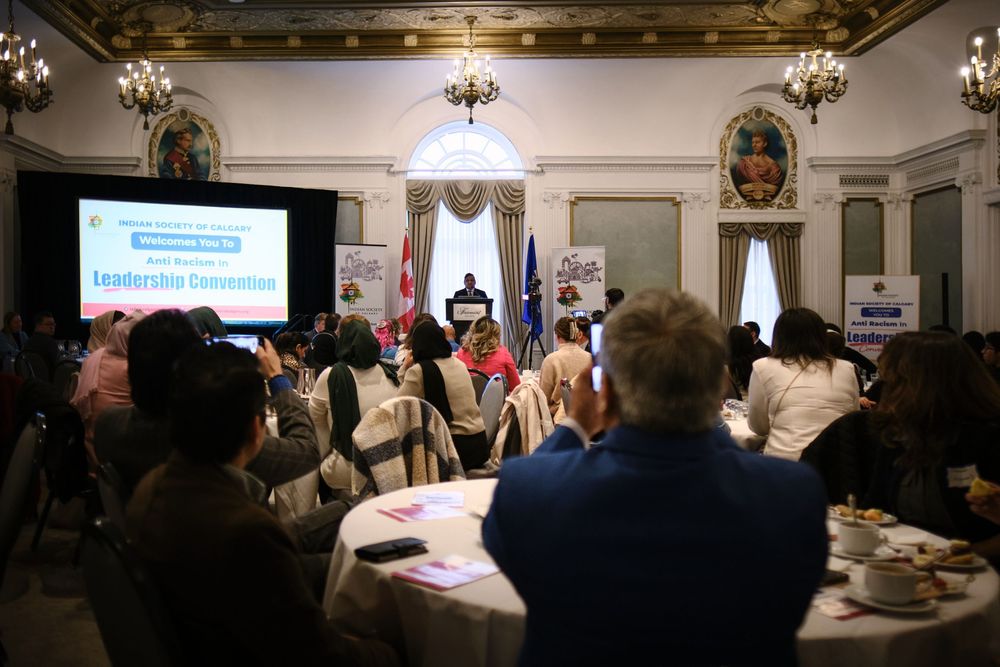Attendees seated at round tables during a leadership convention in an elegant hall with a speaker at the podium.