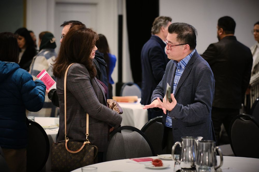Professionals networking at a conference event, engaged in conversation around tables in a modern venue.