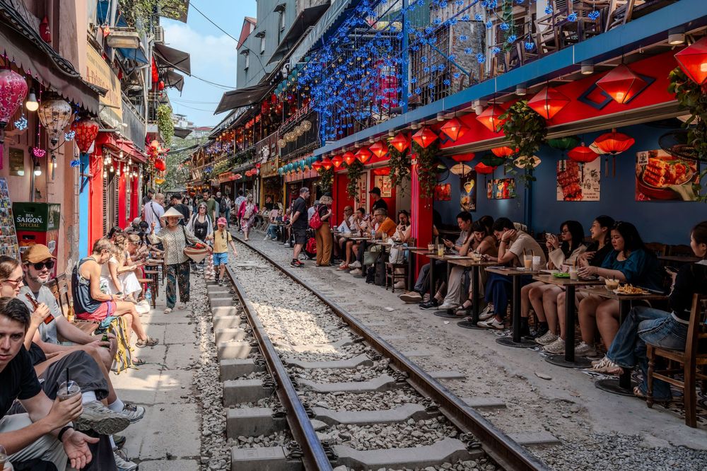 Tourists dining alongside an active railway track in Hanoi's famous Train Street, lined with red lanterns.