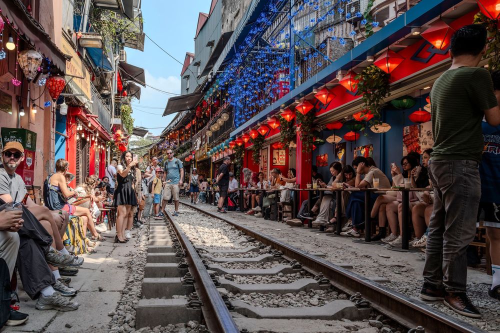 Tourists sit along Hanoi Train Street, lined with red lanterns and cafes, as railway tracks run through the narrow alley.