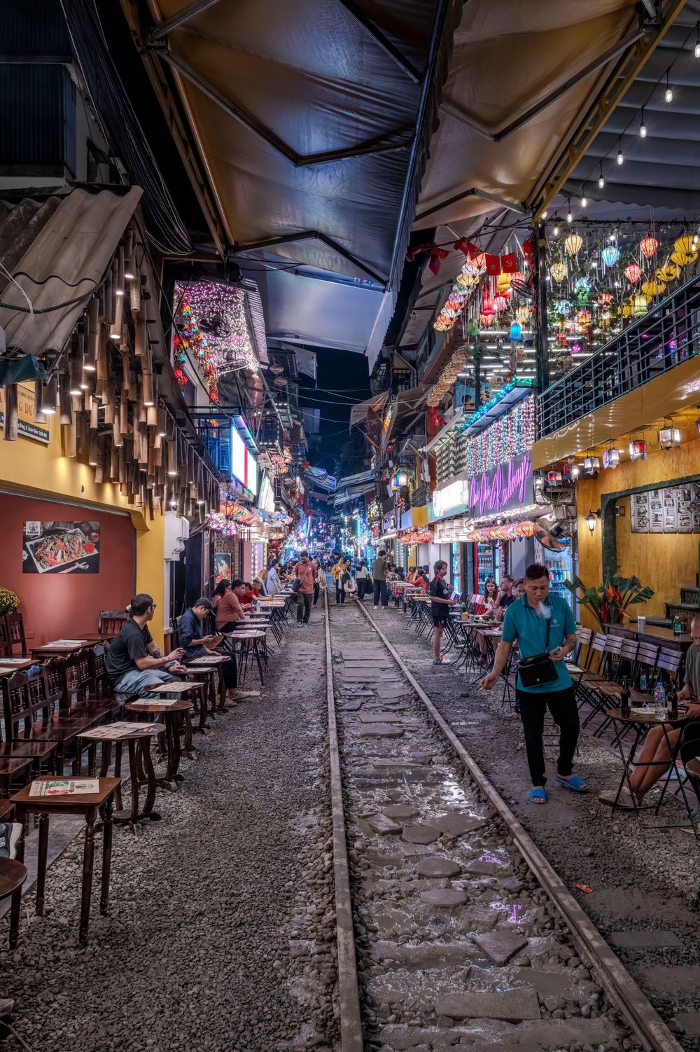 Hanoi Train Street at night with colorful lanterns, cafes, and railroad tracks running through a narrow alley.