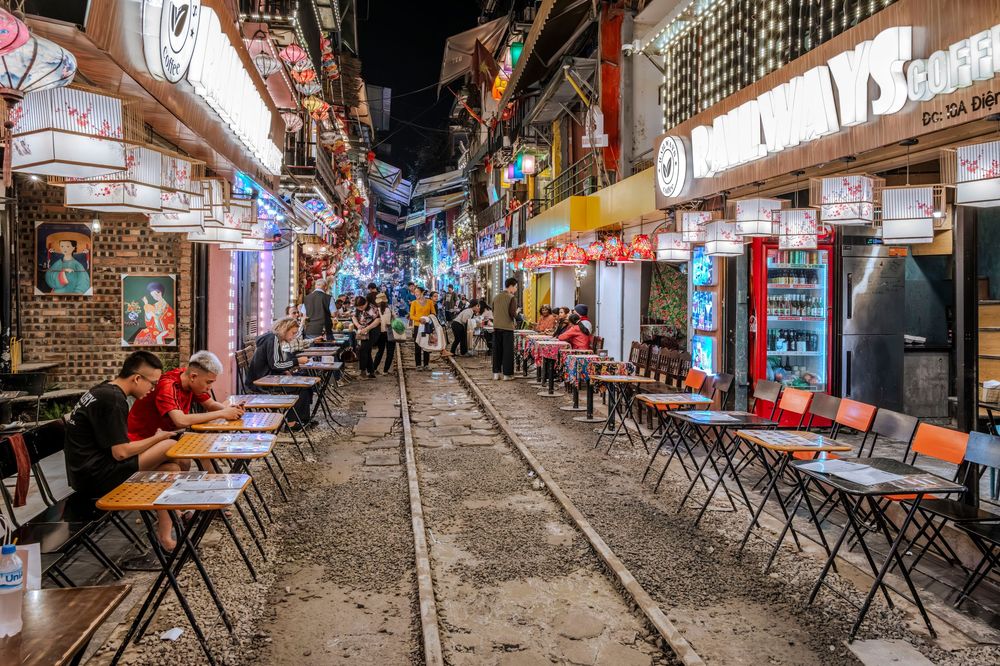 Vibrant train track street lined with outdoor restaurants and colorful signs at night in Hanoi, Vietnam.