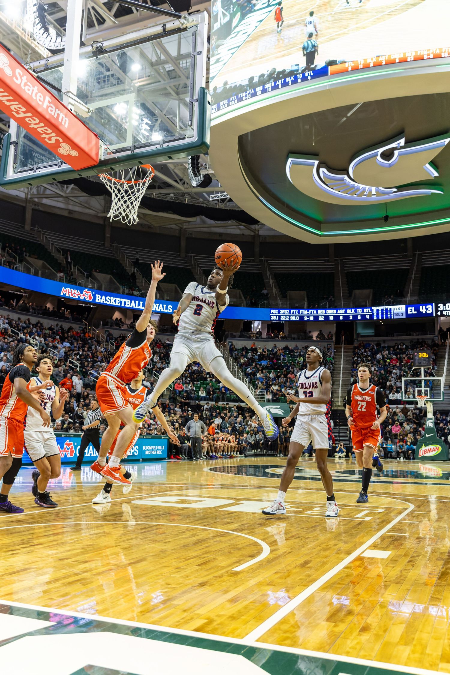 Basketball player in white uniform leaps toward hoop during MHSAA Basketball Finals game in packed arena.