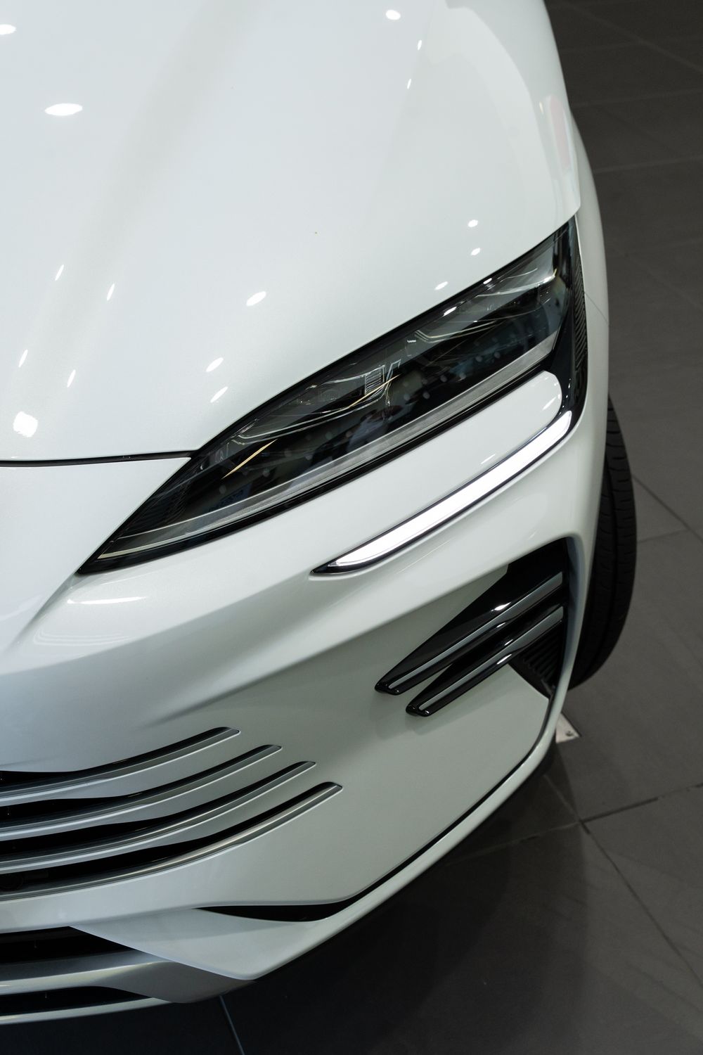 Close-up of sleek white car front headlight with modern LED daytime running light design.