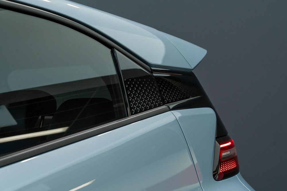 Close-up of light blue car rear quarter panel showing honeycomb vent and red tail light.