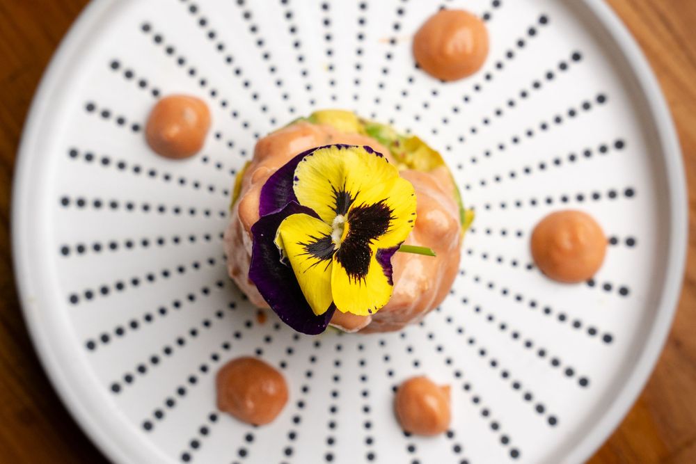 Elegant dessert topped with yellow and purple pansy flower on white dotted plate.