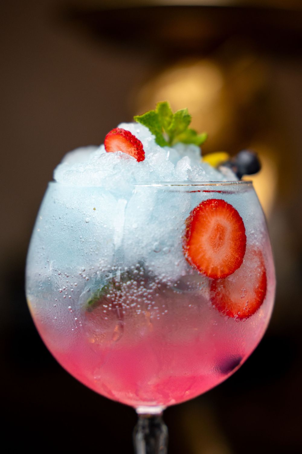 Colorful berry cocktail in large balloon glass with crushed ice, strawberries, blueberries and mint.