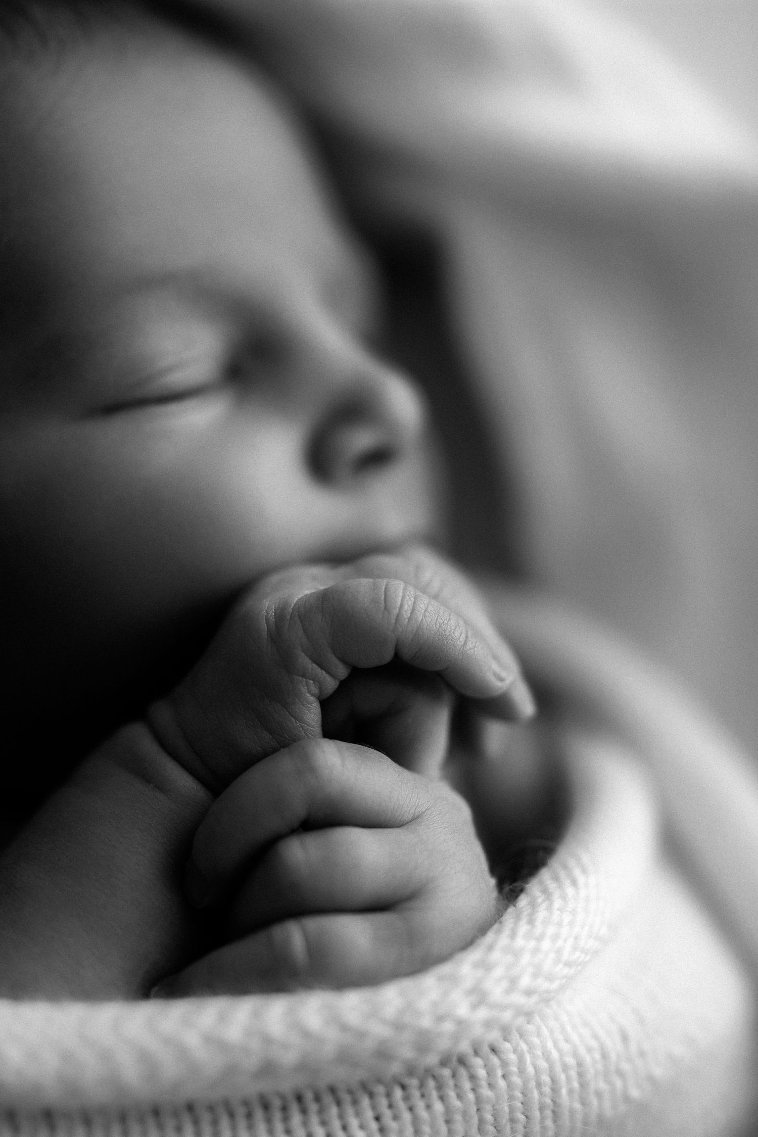 Newborn baby peacefully sleeping on cream colored linens wearing a white romper.