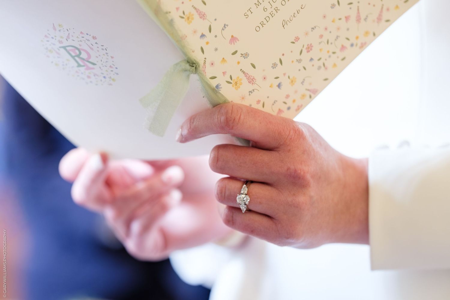 Close-up of a diamond engagement ring on a woman's hand holding wedding ceremony booklets.