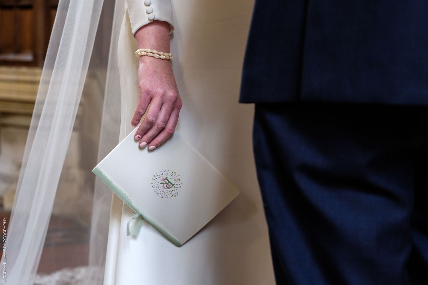 Bride holding a white monogrammed wedding ceremony booklet with gold bracelet detail.