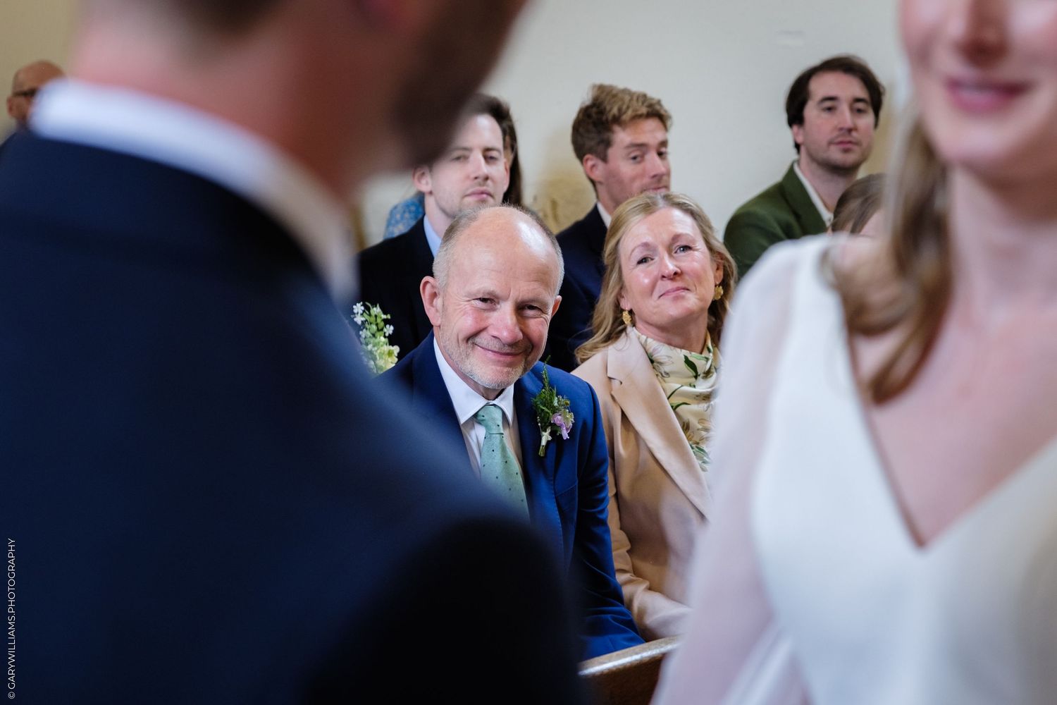 Emotional father smiling proudly at his child during a wedding ceremony while seated in church pews with guests.