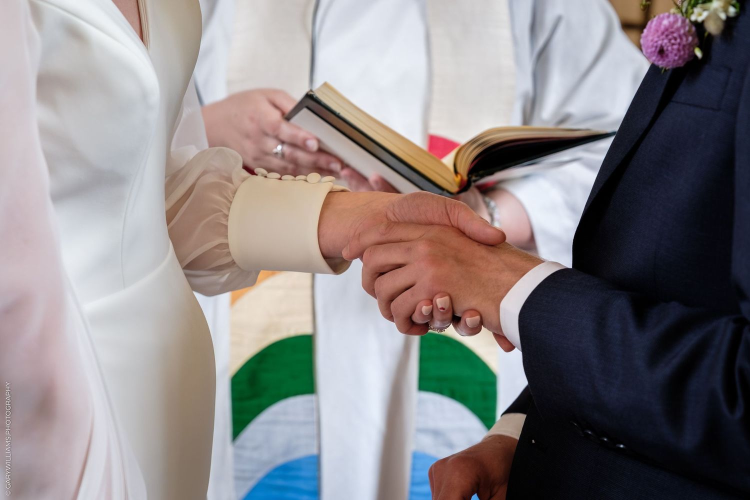 Officiant holds Bible as bride and groom exchange vows and join hands during wedding ceremony.