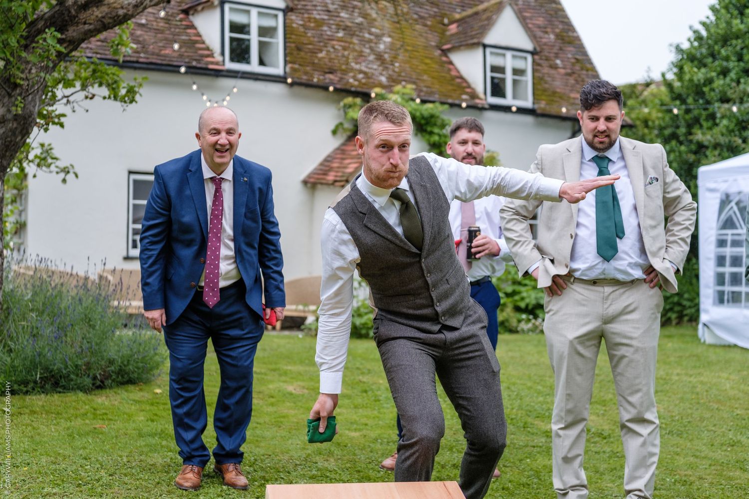 Men playing lawn bowls in suits at a garden wedding reception outside a charming countryside venue.