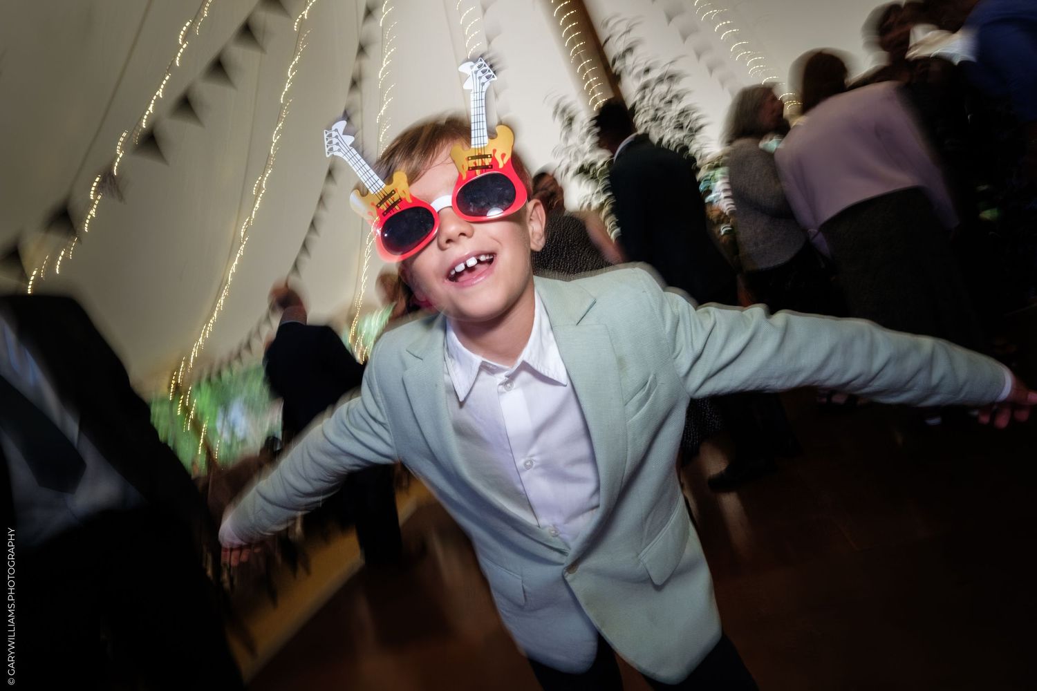 Joyful child wearing oversized novelty glasses and a suit jacket dancing at a festive party celebration.