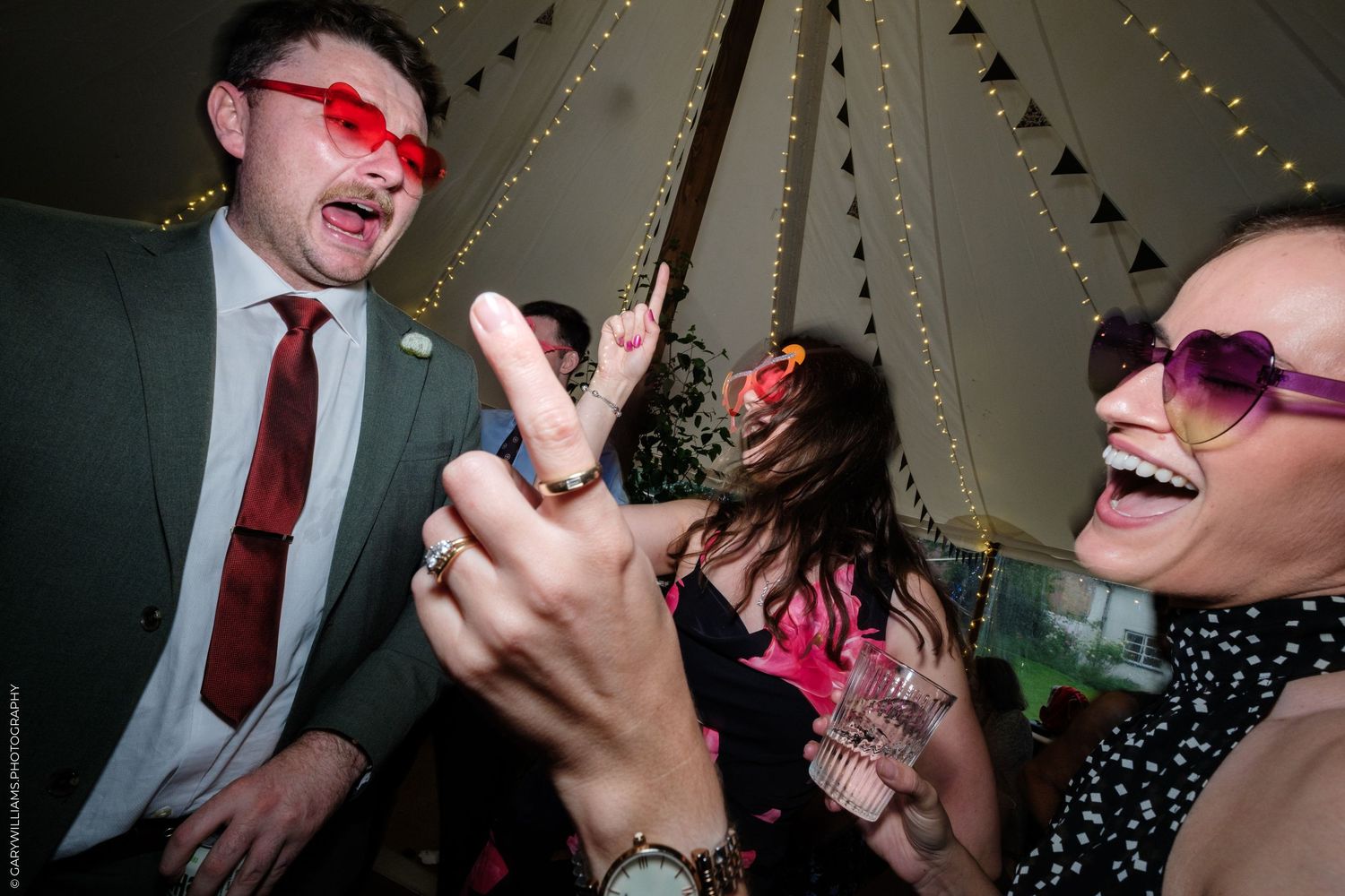 People celebrating at a party in a tipi tent, wearing fun sunglasses and laughing.