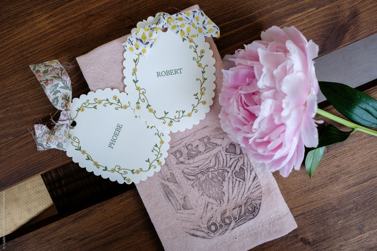 Elegant wedding place cards with floral details beside a pink peony on a wooden table.