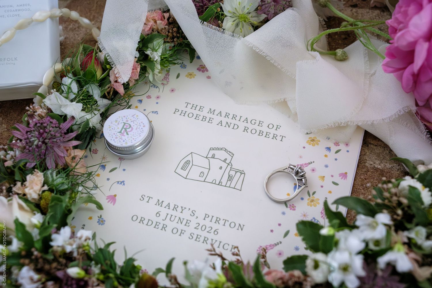 Wedding order of service booklet for Phoebe and Robert at St Mary's Pirton, surrounded by flowers and a diamond ring.