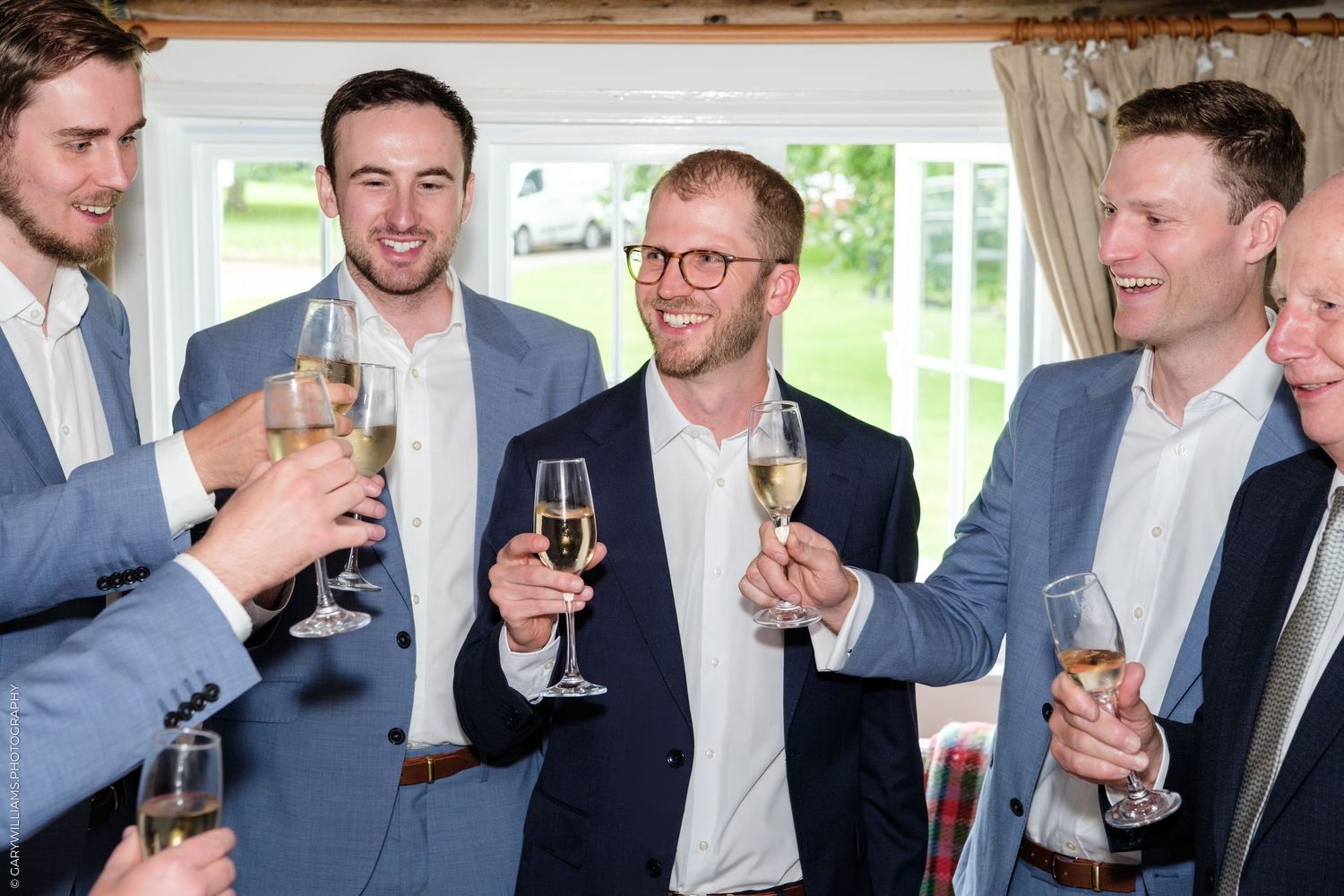 Group of men in blue suits toasting with champagne glasses at a wedding celebration indoors.