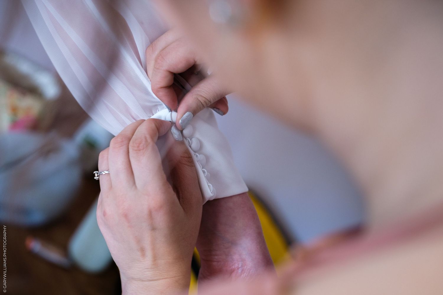 Close-up of hands carefully fastening delicate buttons on a white wedding dress before the ceremony.