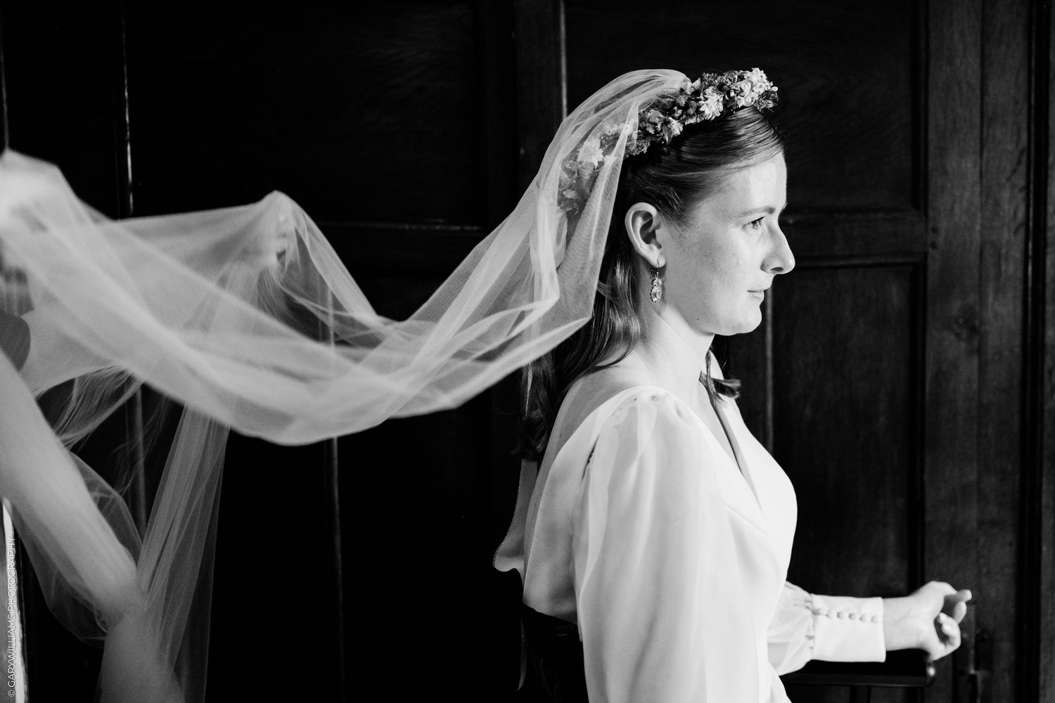 Black and white photo of a bride in a white dress and floral crown, with her veil flowing gracefully behind her.