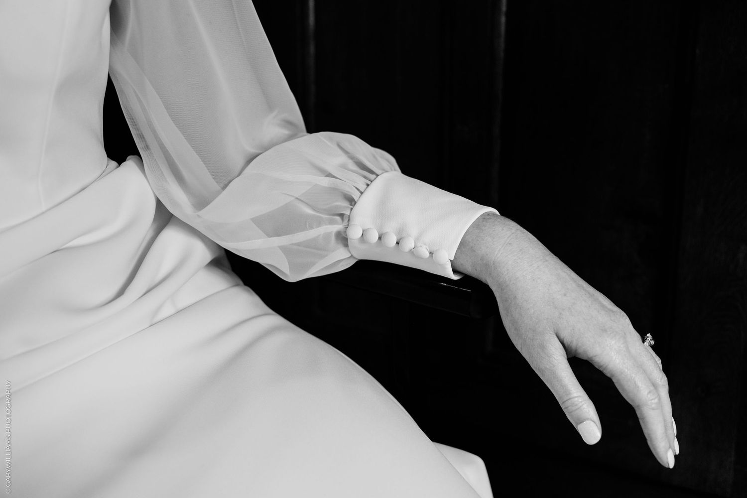 Black and white photo of a bride in a white dress with sheer sleeves, elegant hands resting gracefully.