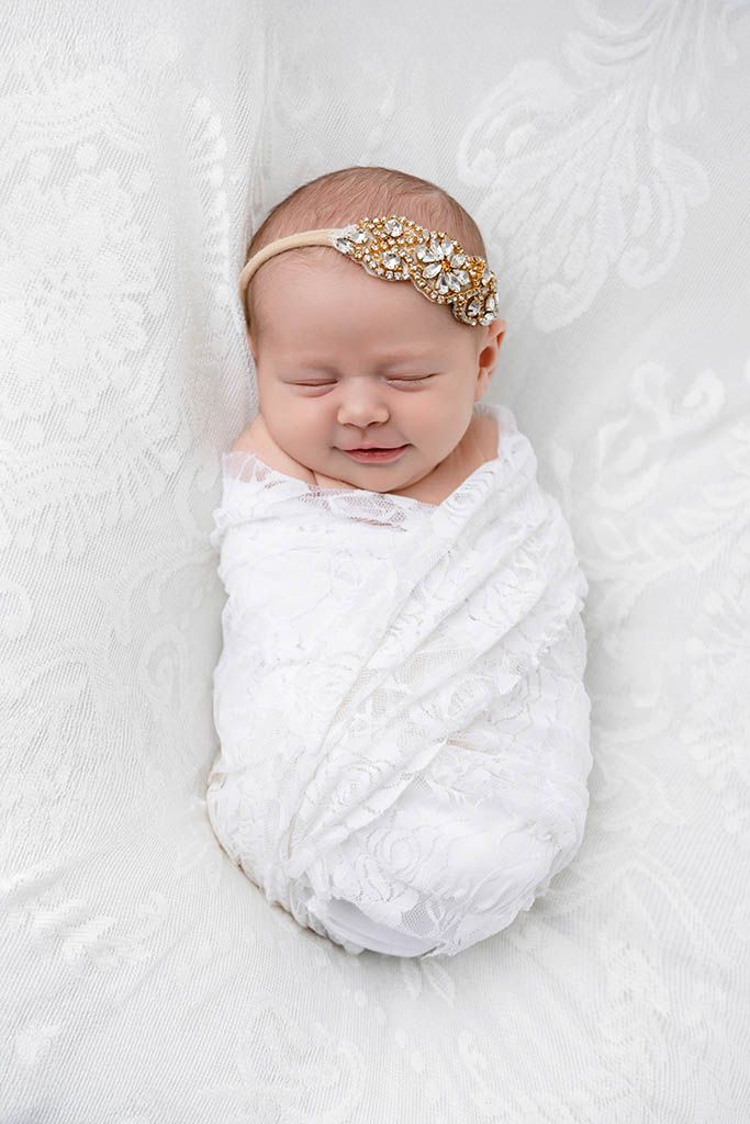 Newborn baby girl swaddled in white lace wrap with gold jeweled headband by Winchester 2 month old baby photographer.