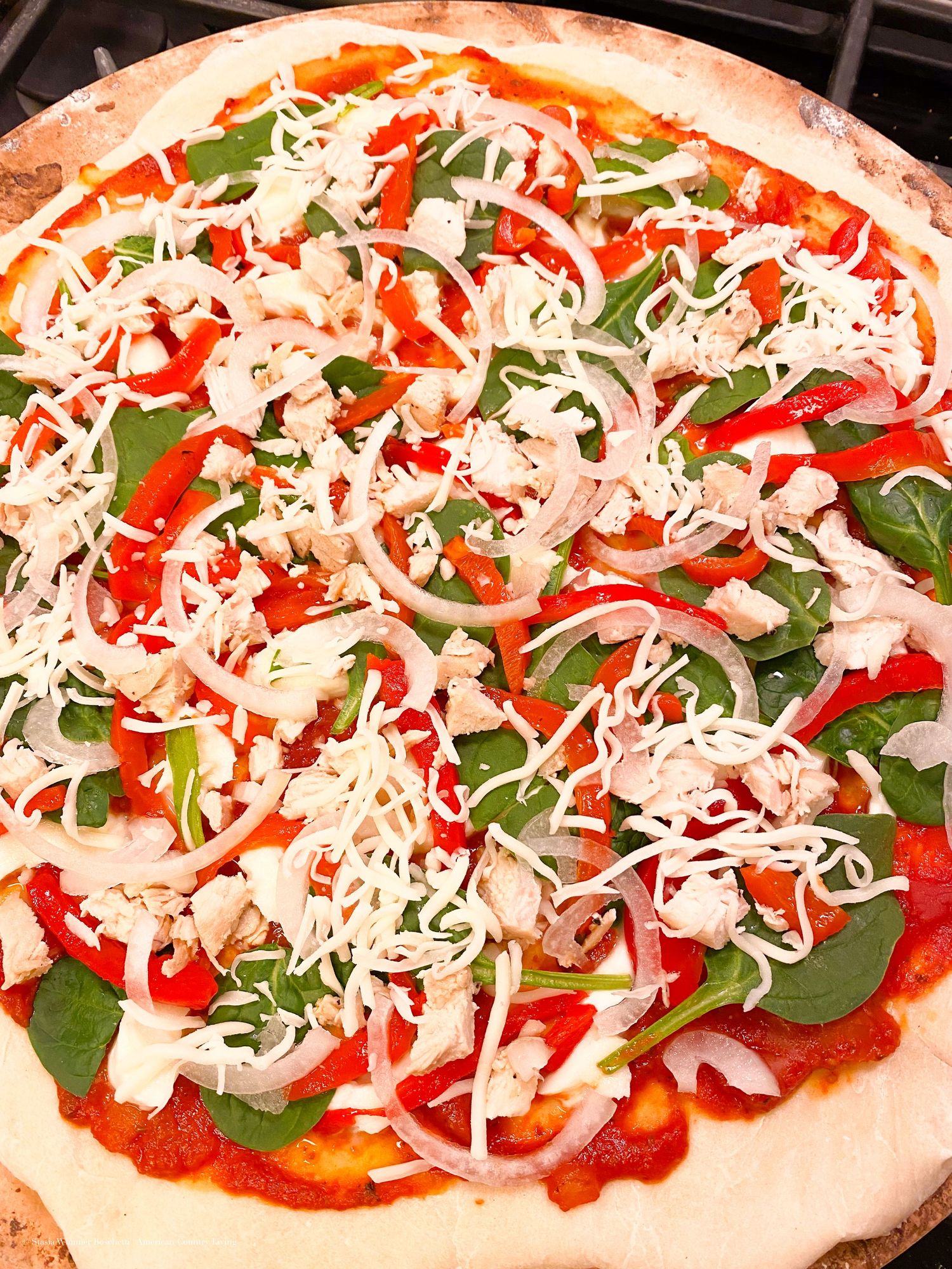 Homemade pizza topped with fresh spinach, red peppers, red onions, feta cheese, and mozzarella on tomato sauce.