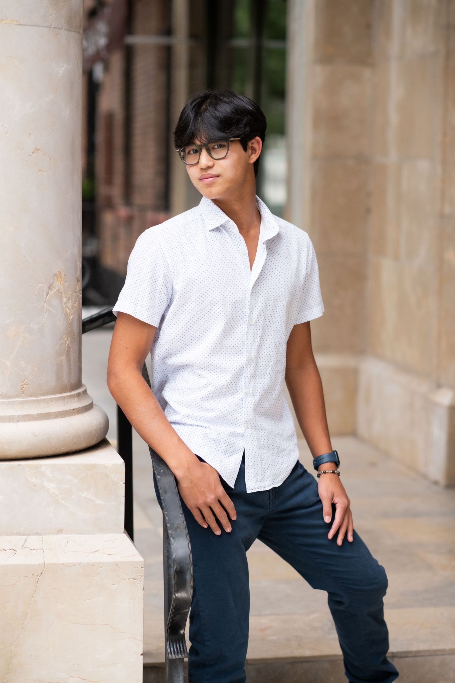 Young Asian teen in white short-sleeve shirt leaning on railing by columns.