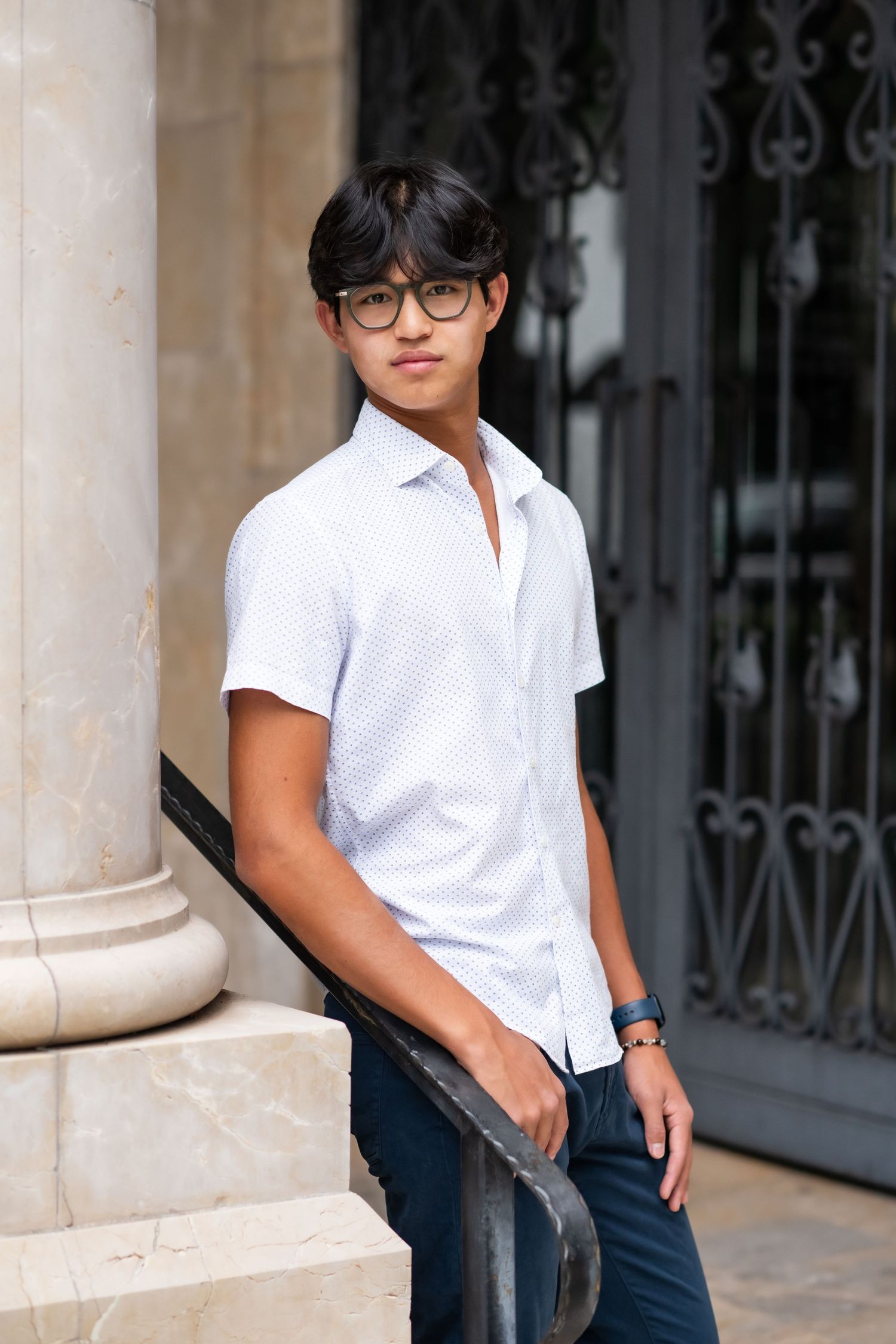 Young man in white short-sleeve shirt leaning on railing beside a marble column.