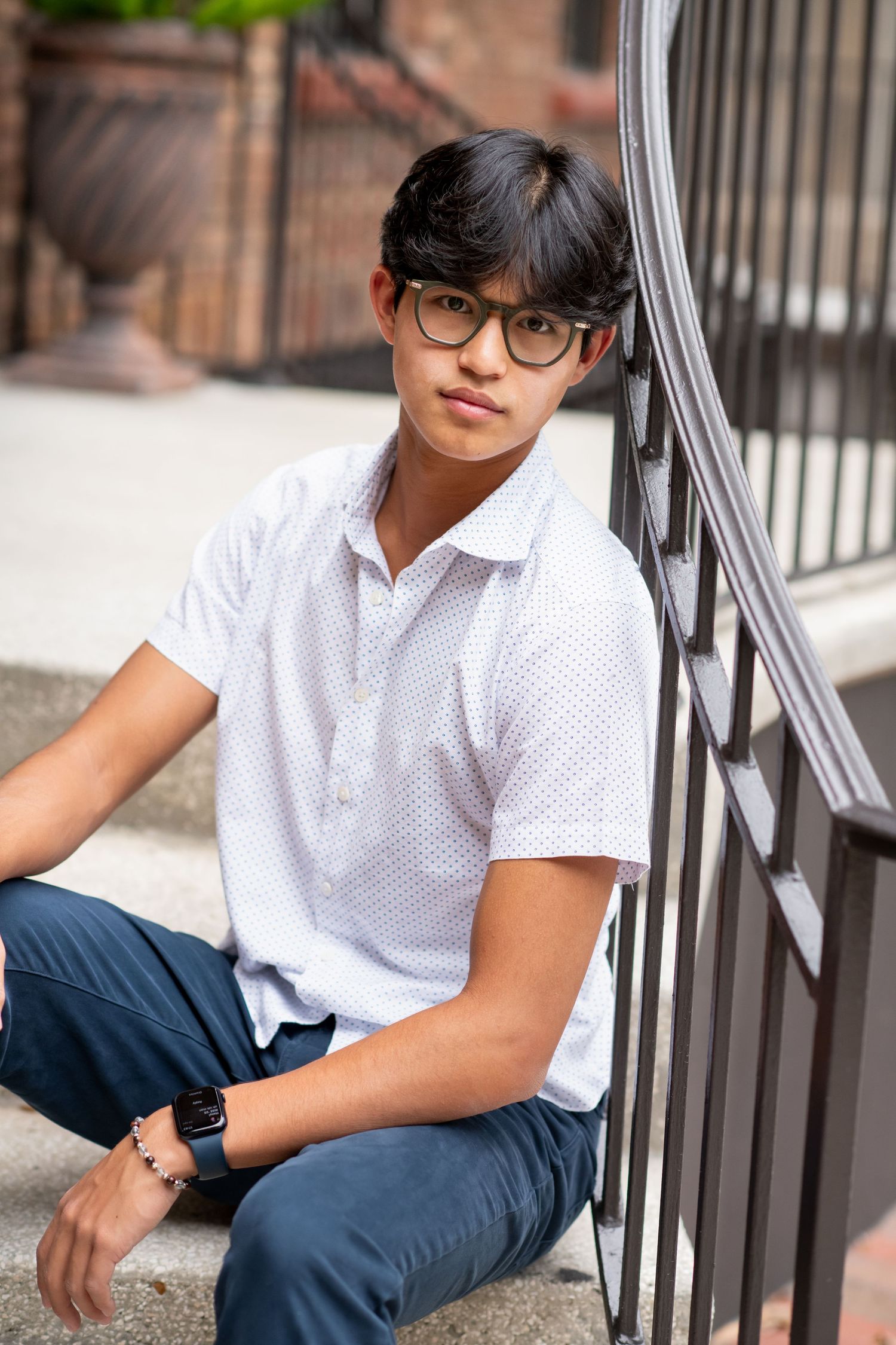 Young man in white polo and glasses leaning on iron railing.