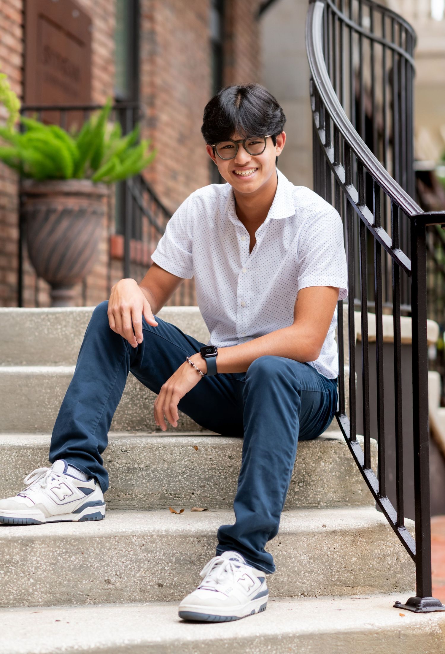 Smiling young man in white polo and navy pants sitting relaxed on brick steps.