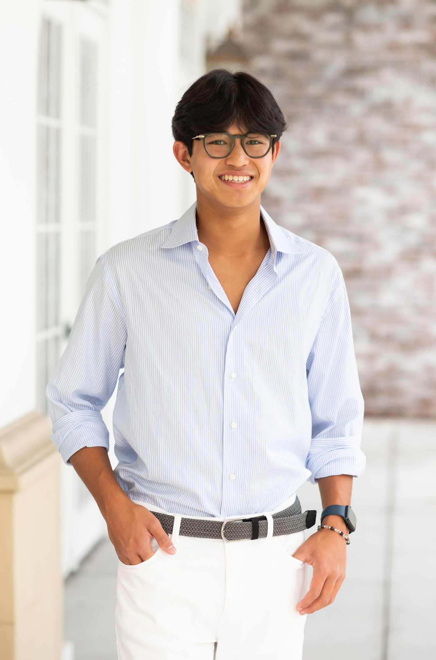 Smiling young man in light blue shirt and white pants poses on outdoor porch.
