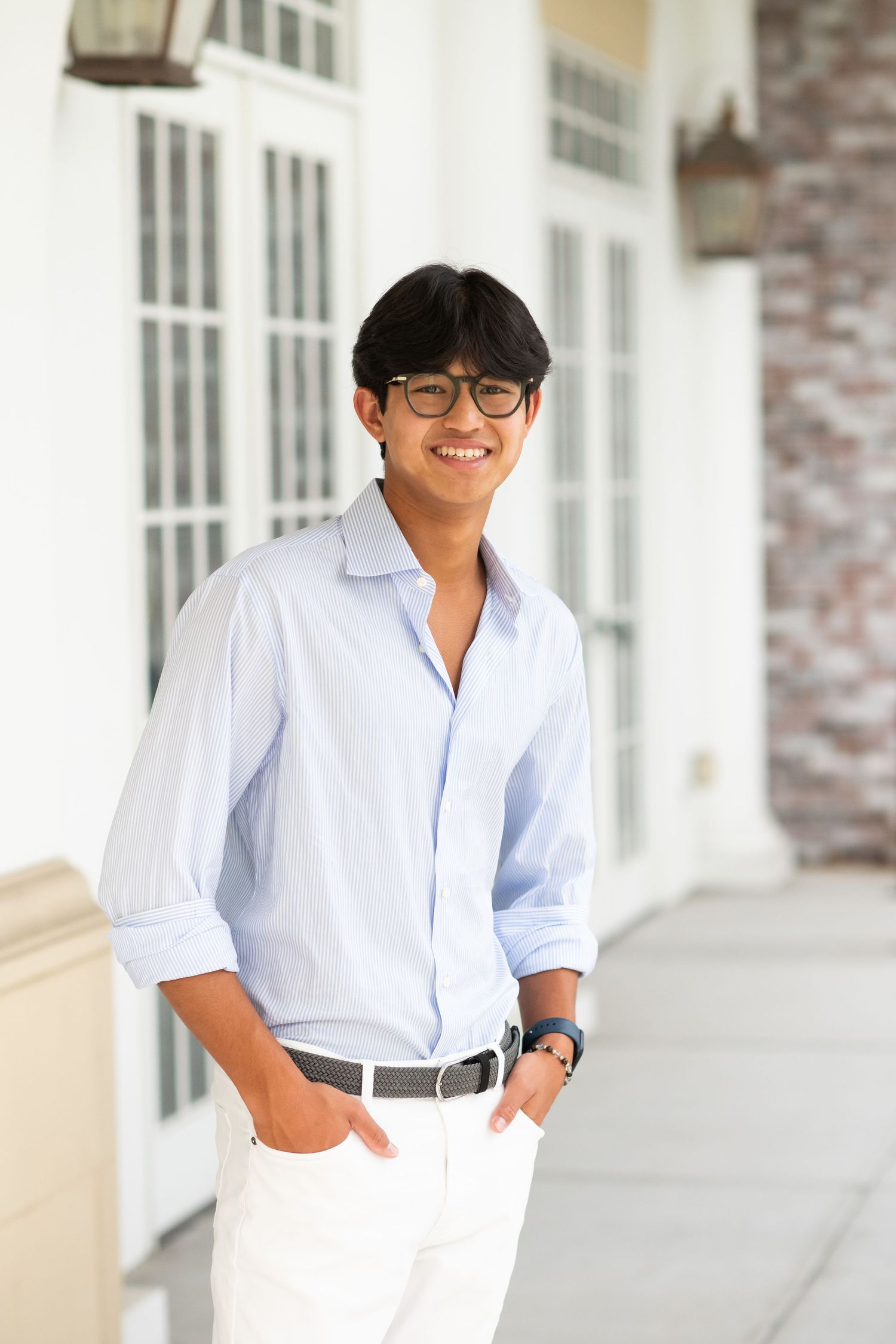 Cheerful young man in light blue shirt and white pants stands on covered porch.