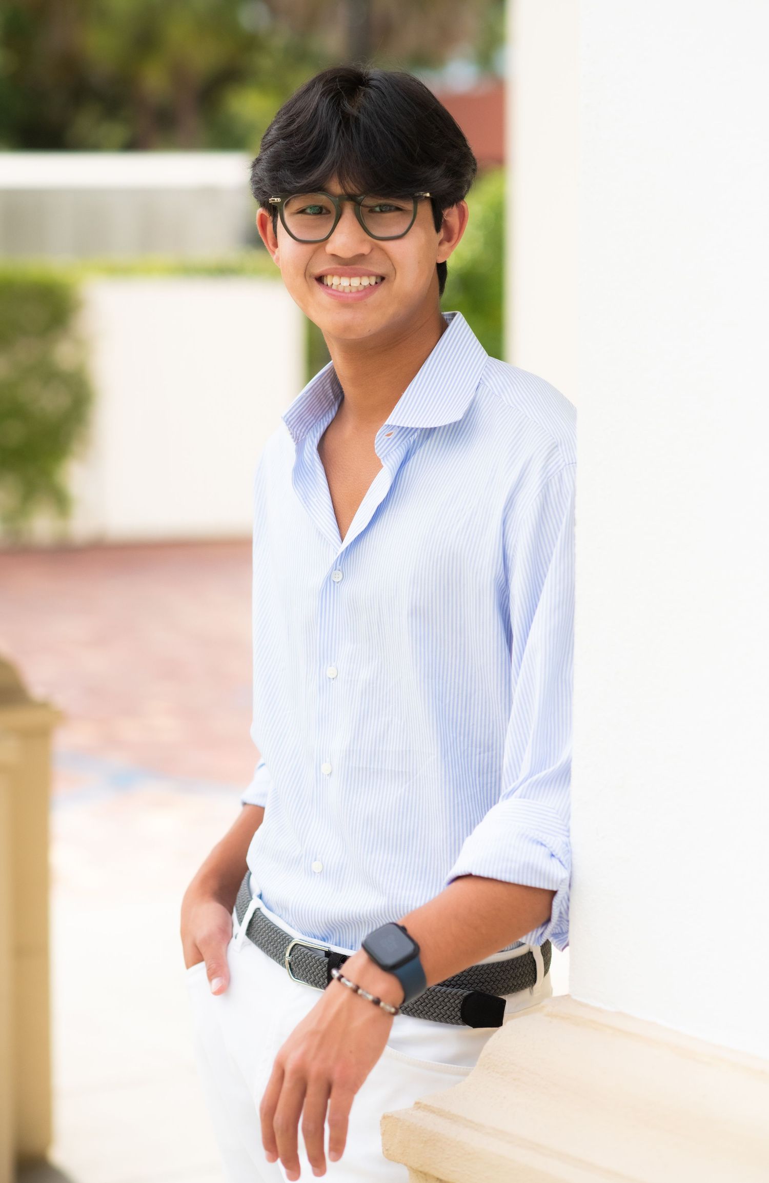 Smiling teen in light blue shirt leaning against white column outdoors.