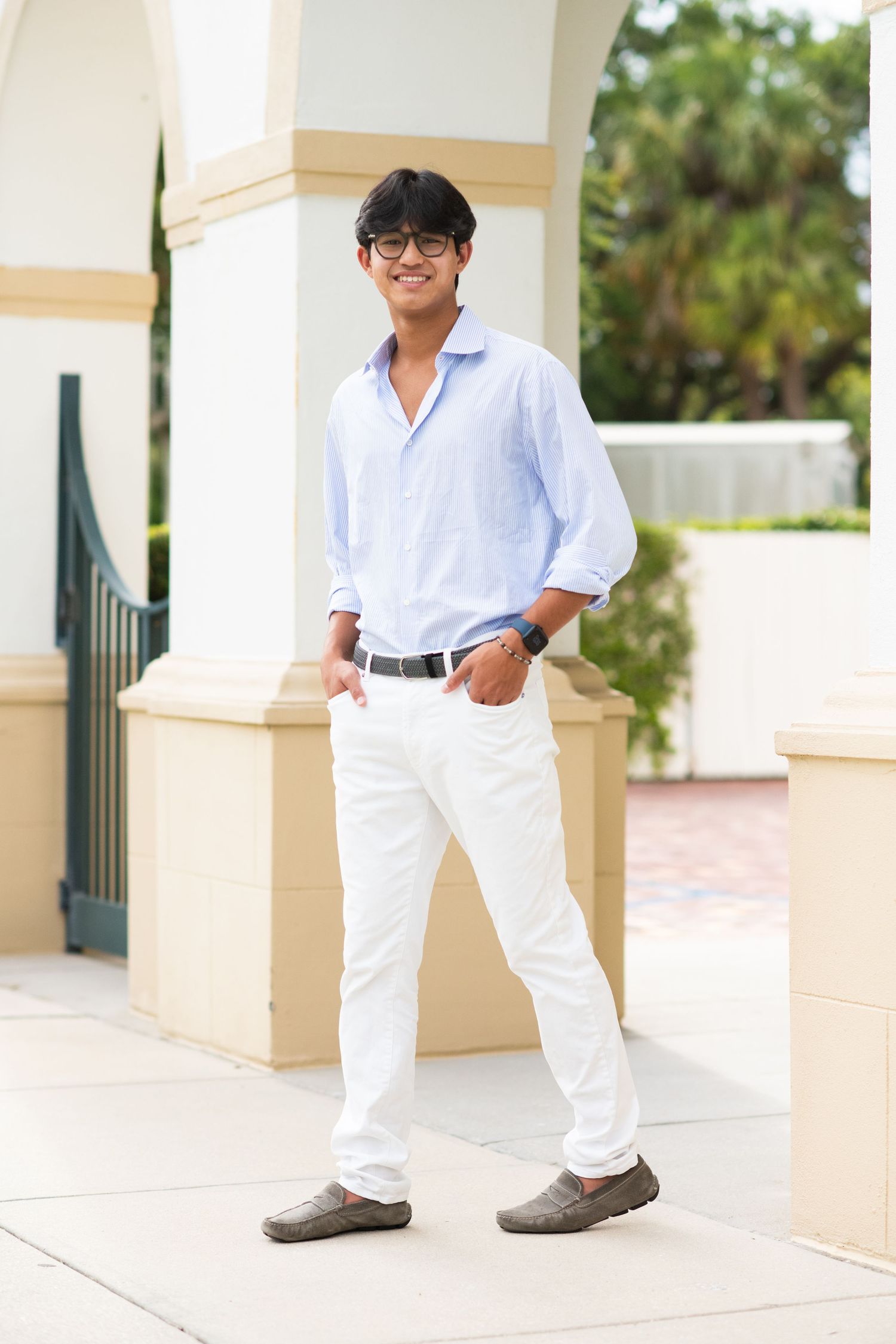 Stylish young Asian man in light blue shirt and white pants standing outdoors smiling.