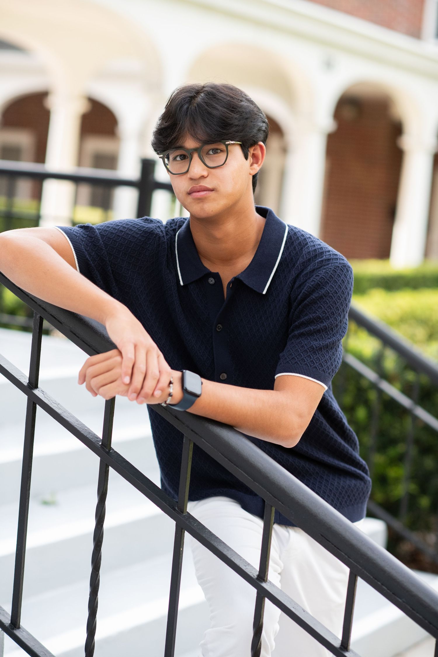 Teen boy in navy polo shirt leaning on black railing at brick building exterior.