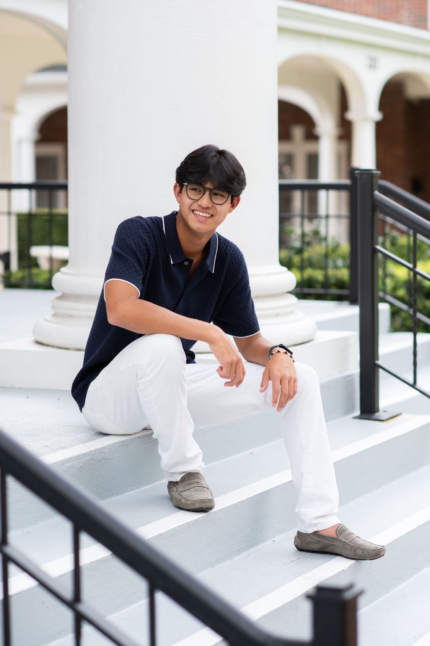 Smiling young man in navy polo and white pants on white steps.