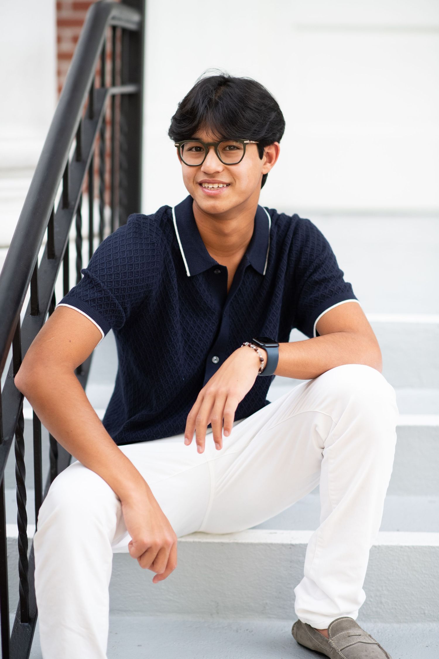 Smiling teen boy in navy polo shirt sits casually on white outdoor steps.