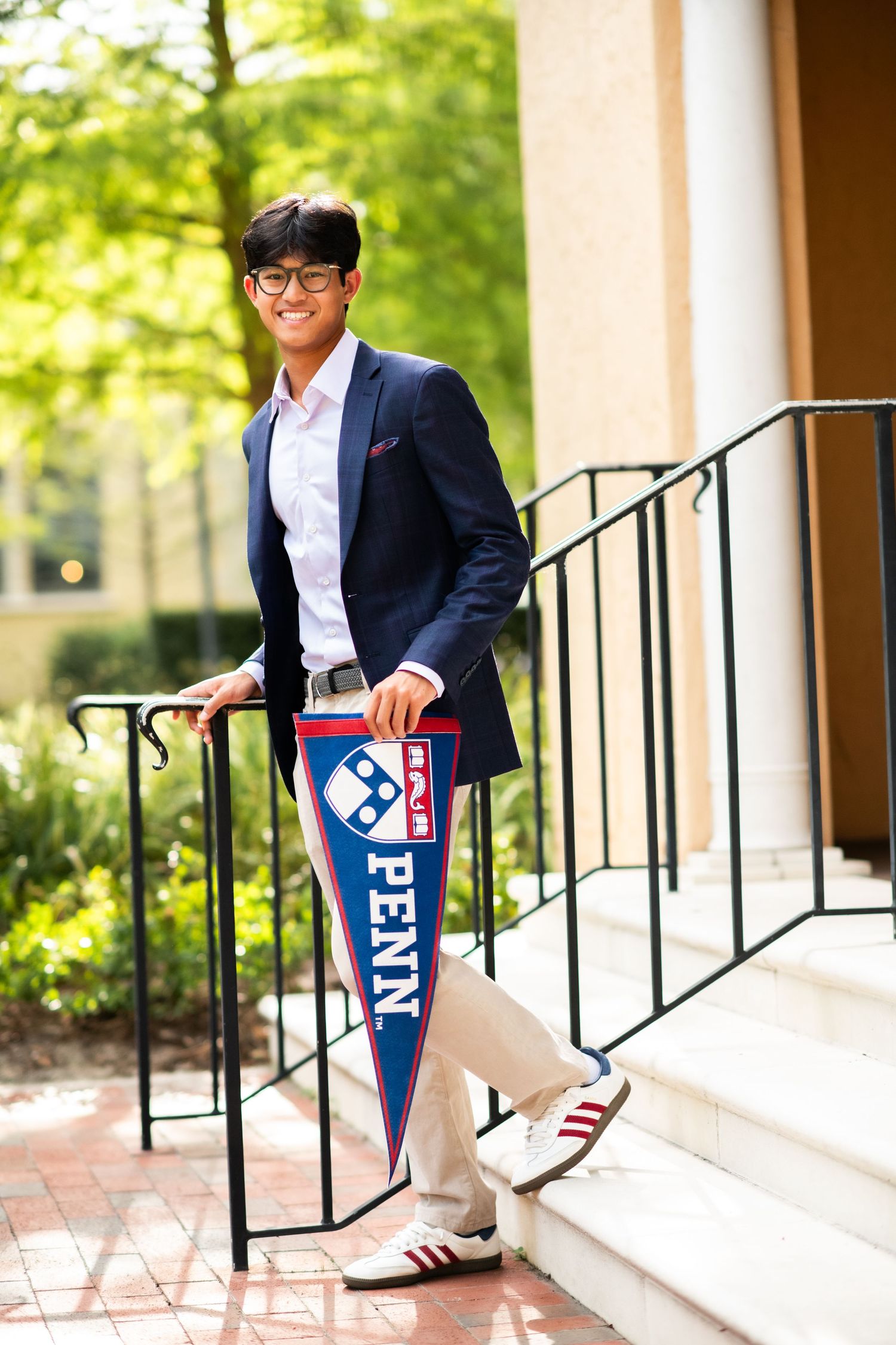 Young man in navy blazer holding a Penn pennant on outdoor steps.